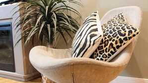 Un sillón moderno con textura tejida, situado junto a una planta grande en maceta y una zona de cocina.