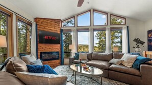 Ein geräumiges Wohnzimmer mit Kamin, Ledersofas, einem Glastisch und einem großen Fernseher, der 'NETFLIX' zeigt.