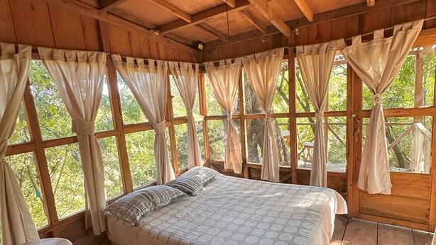 Ein Schlafzimmer in einer Holzhütte mit einem Bett, einem kleinen Tisch und Vorhängen.