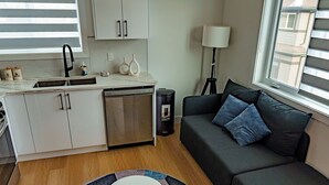 A compact living space with a kitchenette, a sofa with cushions, a lamp, and a window with blinds. - suite, Cozy & Fully Equipped. (Edmonton)