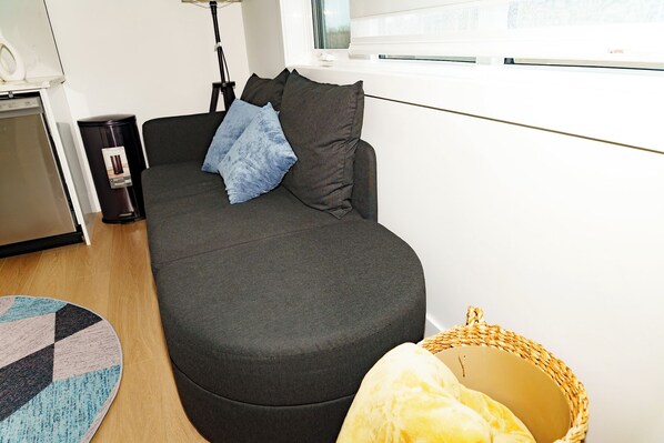A compact living space with a sofa, a trash bin, a lamp, and a window. - suite, Cozy & Fully Equipped. (Edmonton)