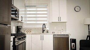 A modern kitchen with white cabinets, a stove, a dishwasher, and a window with blinds. - suite, Cozy & Fully Equipped. (Edmonton)