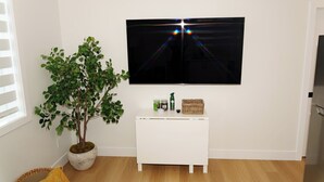 A room with a TV mounted on the wall, a white console table with items, a potted plant, and wooden flooring. - suite, Cozy & Fully Equipped. (Edmonton)