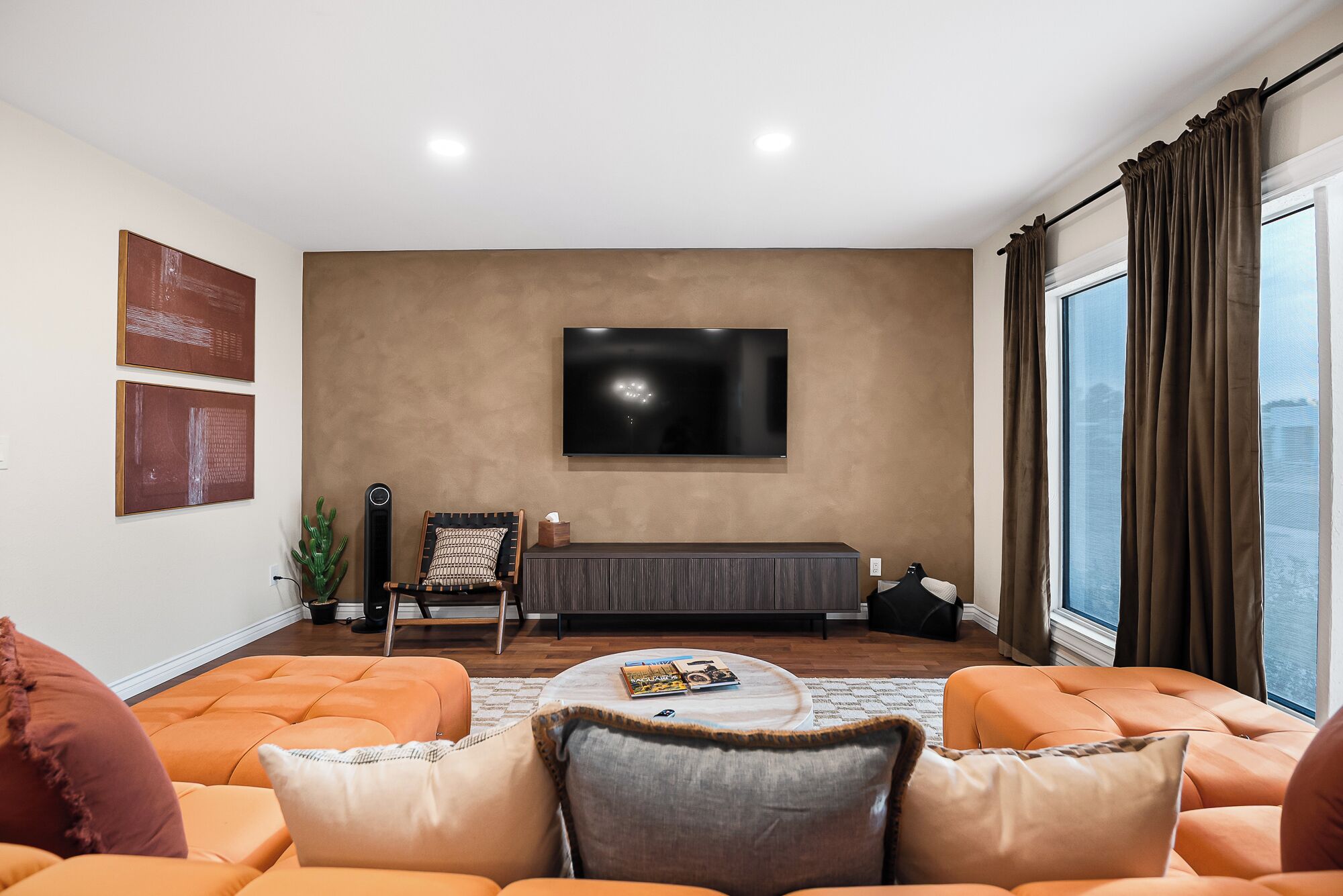 A living room with a large flat-screen TV mounted on the wall, a sofa set, a coffee table, and a window with curtains.