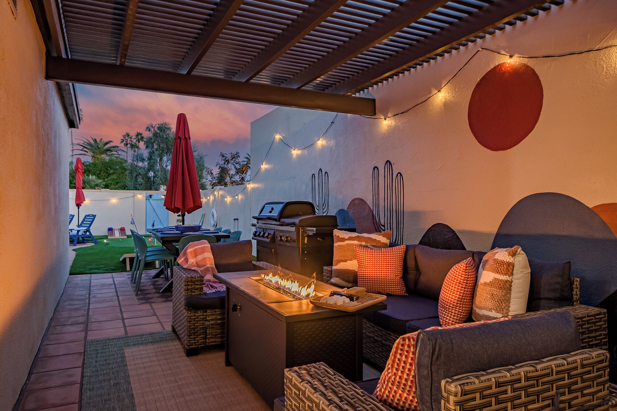 A covered outdoor patio with a grill, lounge chairs, and string lights.
