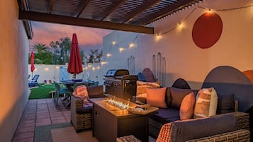 A covered outdoor patio with a grill, lounge chairs, and string lights.