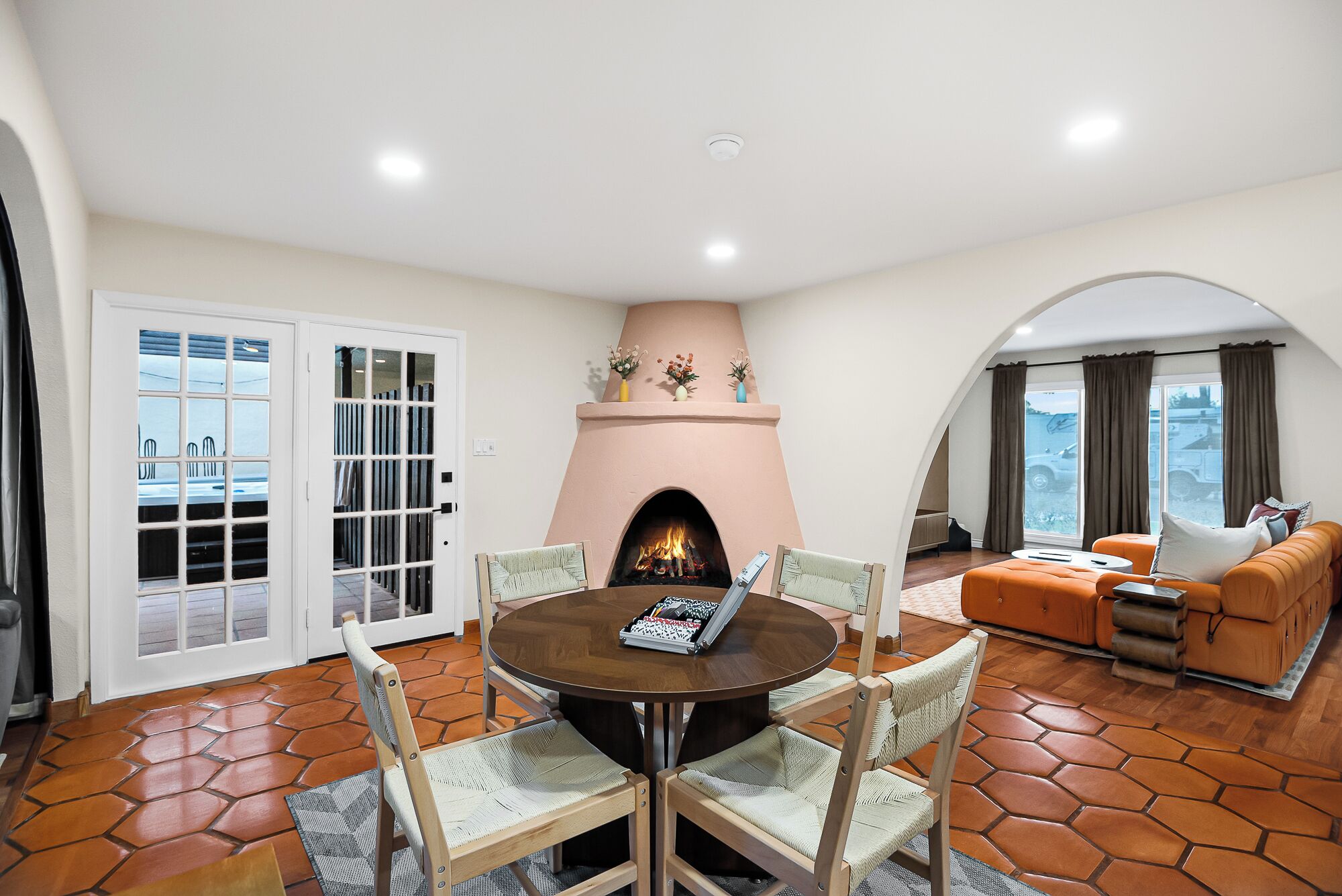 A living room with a fireplace, a dining table with chairs, a sofa, and a view through a window.