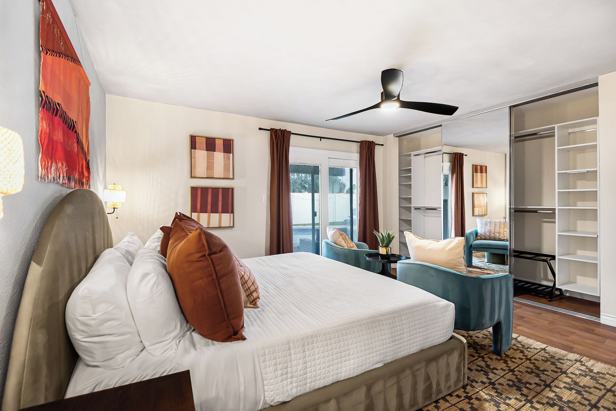 A hotel room with a bed, a desk, a ceiling fan, and a view of the outdoors.