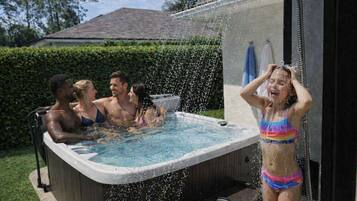 A hot tub with people around it, surrounded by a hedge and a house in the background.