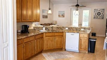 A kitchen with wooden cabinets, granite countertops, a dishwasher, and a ceiling fan.