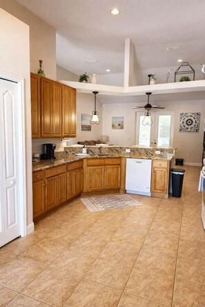 A kitchen with wooden cabinets, granite countertops, a dishwasher, and a ceiling fan.