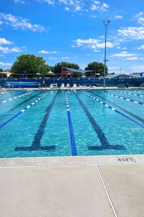 Una piscina con separadores de carril, zona de espectadores cubierta y un alto poste de luz.