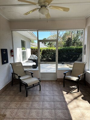 A sunlit room with two chairs, a ceiling fan, and a sliding glass door leading to a patio.