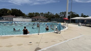 A public swimming pool with multiple lanes, a lifeguard stand, and a covered spectator area.
