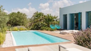 A swimming pool with a wooden deck, a white building with blue shutters, and lush greenery. - Villa Zabbara, independent and private pool (CASTELLAMMARE DEL GOLFO)