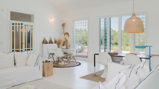 A modern interior with a white sofa, dining table, and chairs, large windows, and a hanging light fixture. - Villa Zabbara, independent and private pool (CASTELLAMMARE DEL GOLFO)