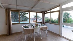 Ett soligt rum med ett bord dukat för två personer, stora fönster och utsikt över en pool och grönområden utanför.