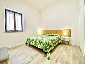 A bedroom with a bed, a nightstand, a lamp, a window with curtains, and a chair. - Riva Marina, on the beach (ALCAMO)
