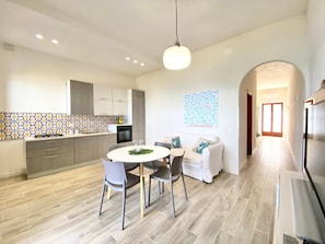 A modern kitchen with grey cabinets, a tiled backsplash, and a round dining table with chairs. - Riva Marina, on the beach (ALCAMO)