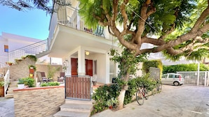 Una casa de dues plantes amb un balcó, una escala que condueix a l'entrada i un cotxe al garatge.