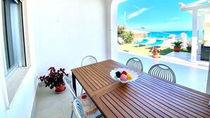 A balcony with a wooden table, chairs, and a bowl of fruit. There is a potted plant on the floor and a view of a pool and outdoor seating area. - Villa dei Gerani, 500 mt from the sea. (ALCAMO)
