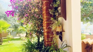 A covered patio area with a brick column, potted plants, and a view of a lush garden. - Casale Bagni Villa with private and independent swimming pool (CANICATTINI BAGNI)