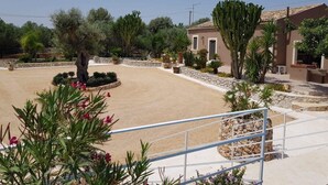 A courtyard with a sandy ground, surrounded by cacti and various plants, with a building featuring a tiled roof in the background. - Casale Bagni Villa with private and independent swimming pool (CANICATTINI BAGNI)