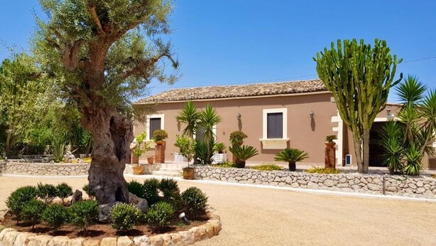 A building with a stone facade, a tiled roof, and a landscaped garden with a large tree and various shrubs. - Casale Bagni Villa with private and independent swimming pool (CANICATTINI BAGNI)