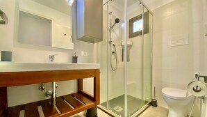 Et moderne badeværelse med en glasafskærmet brusekabine, en trækommode, et hvidt toilet og et spejl over vasken.