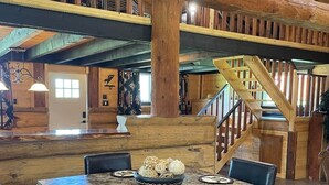Un vaste espace dédié à la salle à manger, avec une grande table et des chaises en bois, un vase décoratif placé au centre, et un escalier menant à un niveau supérieur.