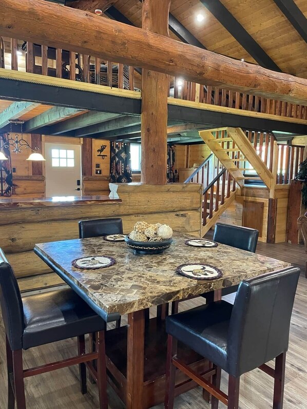 Un comedor espacioso con una gran mesa de madera y sillas, un cuenco decorativo en el centro, y una escalera que sube a un nivel superior.