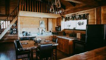 Une cuisine rustique aux murs en bois, un coin repas avec une table et des chaises, et un réfrigérateur.
