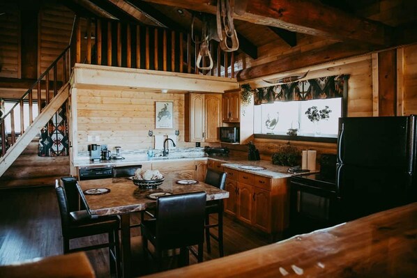 Una cocina rústica con paredes de madera, un comedor con mesa y sillas, y un refrigerador.