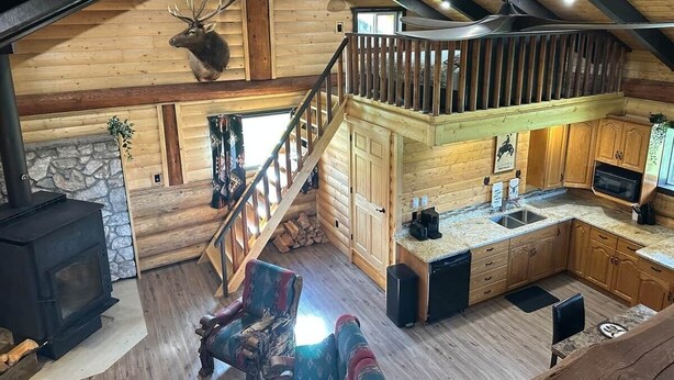 L’intérieur chaleureux d’un chalet, avec un revêtement mural en bois, une cheminée, un coin cuisine et un escalier menant à un étage supérieur.