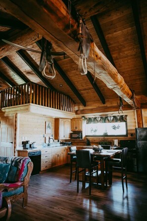 Un interior rústico de madera con comedor, cocina y un altillo con luces colgantes.