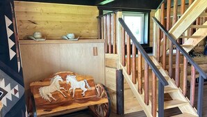 Un intérieur rustique en bois, avec un escalier en bois, un banc orné de sculptures de chevaux et une fenêtre laissant entrer la lumière naturelle.