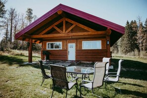 Uma cabana de madeira com mesa e cadeiras de vidro no alpendre.