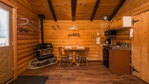 Ein gemütliches Blockhaus mit Holzvertäfelung, Kamin, Esstisch und Küchenzeile.