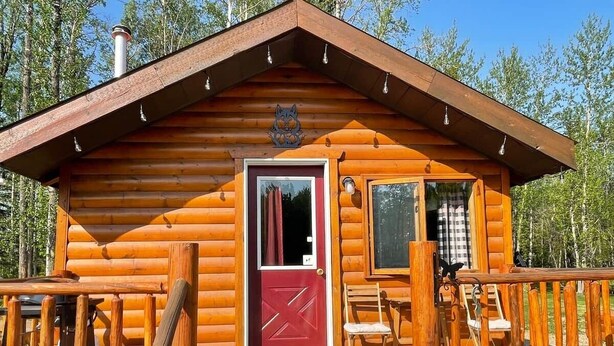 Eine Holzhütte mit roter Tür, einem Balkon und einem Hollerker.