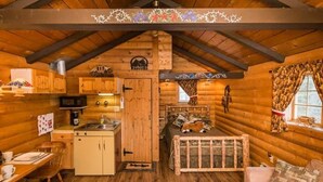 A cozy log cabin interior with a kitchen, dining area, and a bed with a rustic headboard. - The Mustang Cabin - Bear Creek Cabins (County Of Wetaskiwin No. 10)