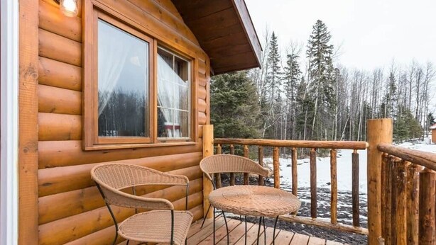A wooden cabin with a deck, two wicker chairs, and a table. - The Mustang Cabin - Bear Creek Cabins (County Of Wetaskiwin No. 10)