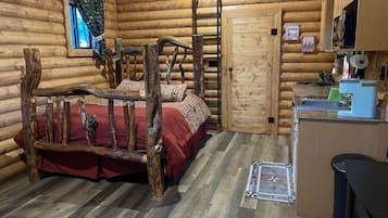 Quarto de cabana rústica com cama de madeira, um pequeno espaço para cozinha e janela com cortinas.
