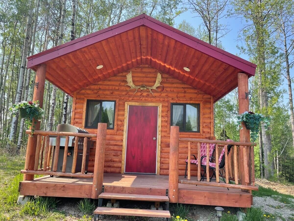 Eine Holzhütte mit roter Tür, einer Veranda mit Geländer und zwei Fenstern.
