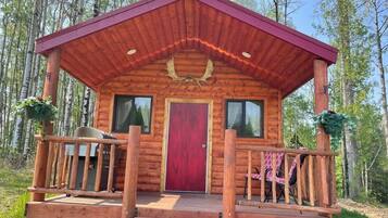 A wooden cabin with a red door, a porch with a railing, and two windows.