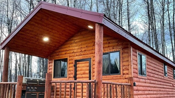 Una cabaña de troncos con porche y zona de barbacoa.