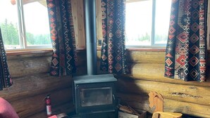 Ein gemütliches Blockhaus-Interieur mit Holzofen, Schaukelstuhl und einem roten Polsterstuhl.