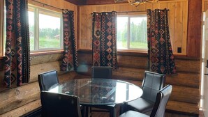 Ein Holzhütten-Interieur mit einem runden Glastisch, Ledersesseln, gemusterten Vorhängen und einer Chandelüster.
