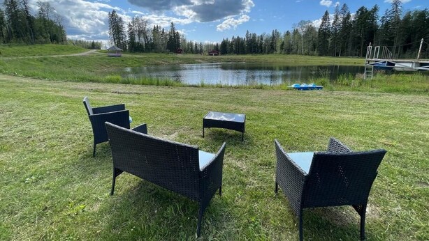 Eine grüne Außenanlage mit vier Korbstühlen und einem kleinen Tisch, einem Teich und Booten im Hintergrund.