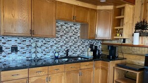 Eine Küche mit Holzausstattung, einer schwarzen Arbeitsplatte und einer Mosaik-Spritzschutzleiste.