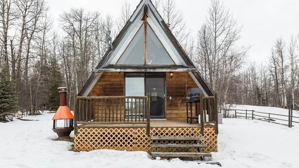 A wooden cabin with a triangular roof, a front porch with a lattice railing, and a chimney.